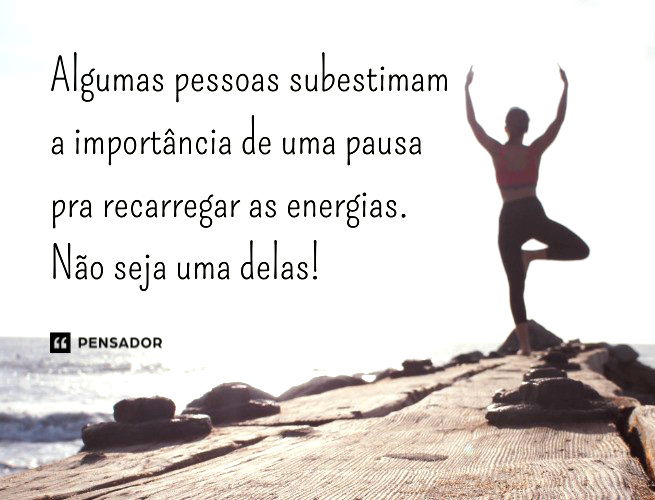 Mulher com uma perna dobrada sobre a outra, fazendo uma posição de exerício em cima de uma pedra na praia. Ela ergue as mãos abertas ao ´´ceu.